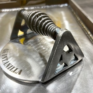 May include: A silver metal grill press with a spring-loaded handle and a circular base with the word "Quintanilla" engraved on it.