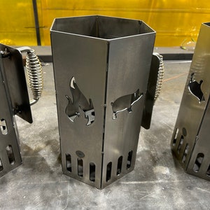 May include: Two metal charcoal chimney starters with a pig and flame design. The chimney starters are made of sturdy metal and have a handle for easy carrying.
