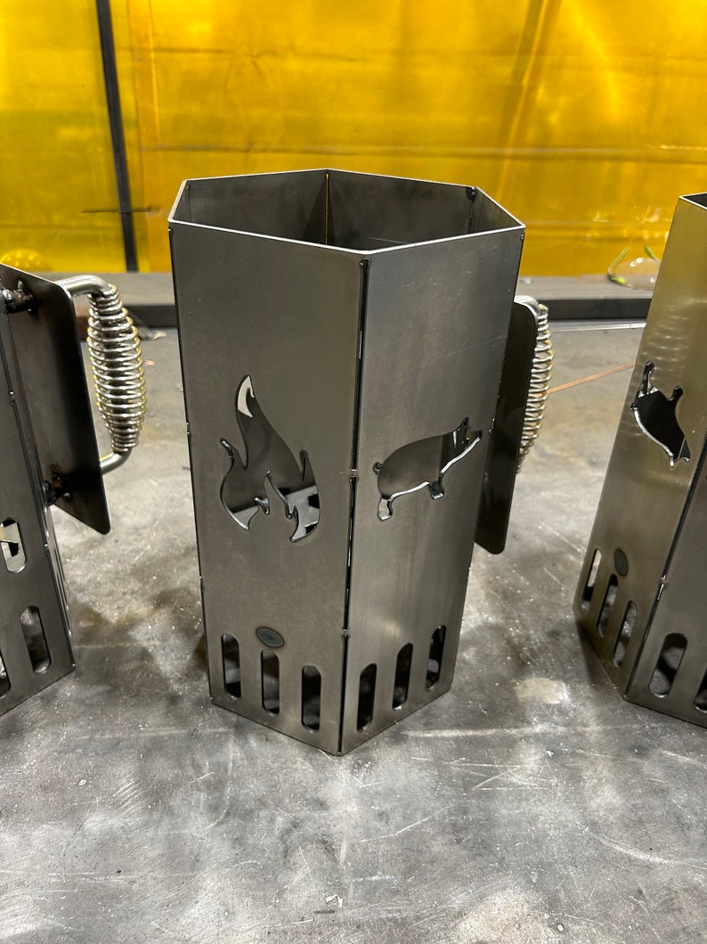 May include: Two metal charcoal chimney starters with a pig and flame design. The chimney starters are made of sturdy metal and have a handle for easy carrying.