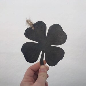 May include: A black metal four-leaf clover cutout with a twine loop for hanging.