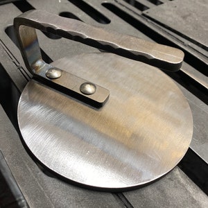 May include: A round, metal pizza stone with a handle. The stone has a brushed finish and is made of durable metal.
