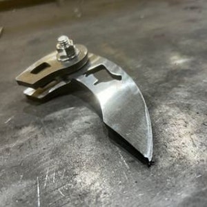 May include: A silver metal curved piece with a hole in the centre and a bolt attached to the top. The piece has a smooth, polished finish.