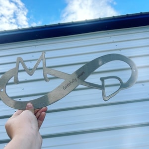 May include: A silver metal infinity symbol with the letters "M" and "D" cut out and the words "Faithfully yours" engraved on the top.