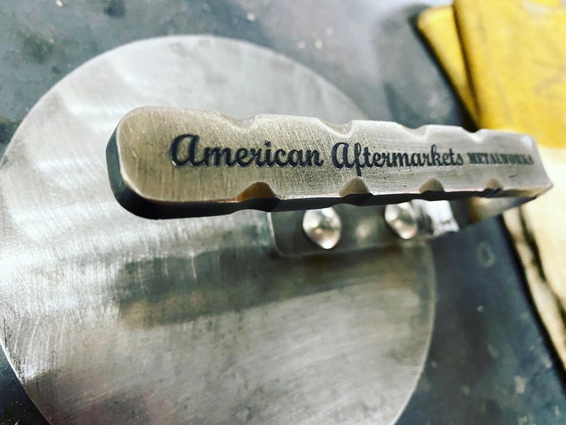 May include: Close-up of a metal handle with the text "American Aftermarkets Metalworks" engraved on it.