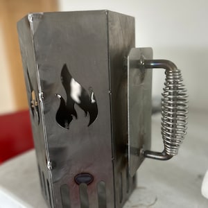 May include: A metal charcoal chimney starter with a spring-loaded handle and a flame cutout design.