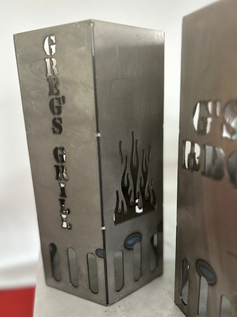 May include: Two metal fire pit stands with cut-out flames and the words "Greg's Grill" and "G's BBQ" on the front.