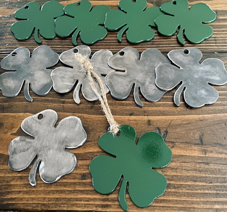 May include: A set of metal four-leaf clover ornaments, some painted green and some with a distressed silver finish. The ornaments are strung together with twine.