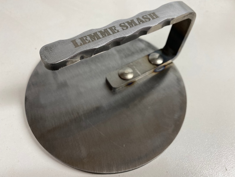 May include: A silver metal burger smasher with a handle that says "LEMME SMASH".