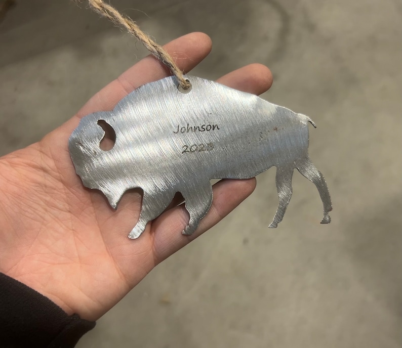 May include: Metal ornament shaped like a buffalo with the name "Johnson" and the year "2023" engraved on it.