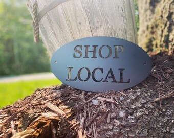 May include: Black metal oval sign with the text "SHOP LOCAL" in white lettering.