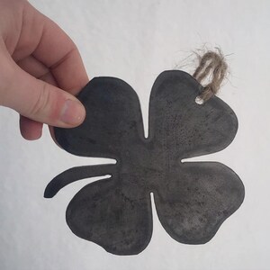 May include: A four-leaf clover shaped metal ornament with a rustic finish and a twine hanger.