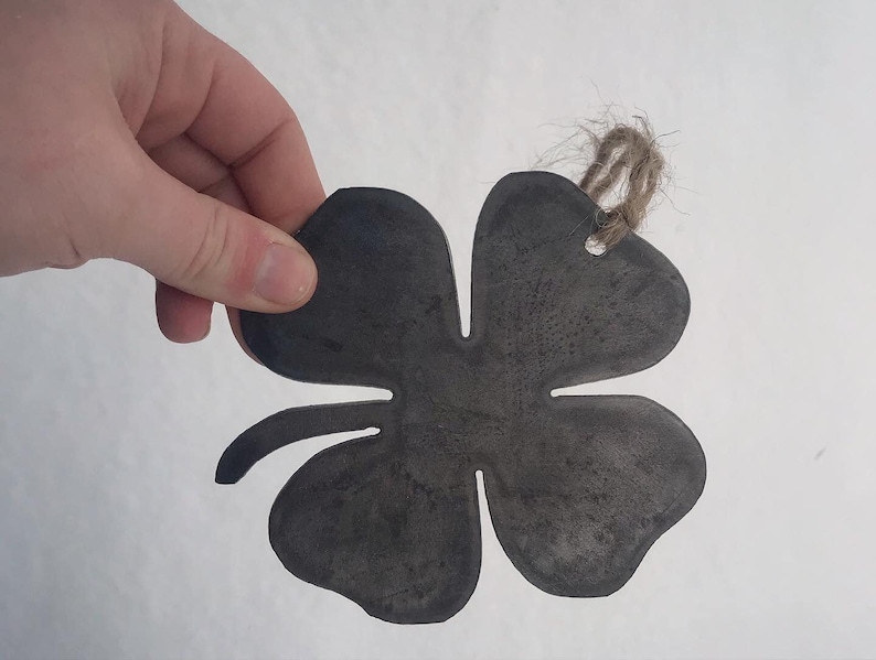 May include: A four-leaf clover shaped metal ornament with a rustic finish and a twine hanger.