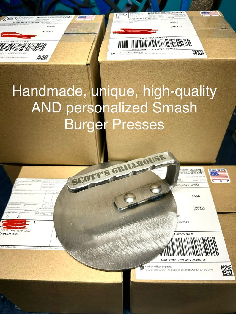 May include: A stainless steel smash burger press with a handle and the words "SCOTT'S GRILLHOUSE" engraved on the top. The press is sitting on top of a cardboard box with a shipping label.