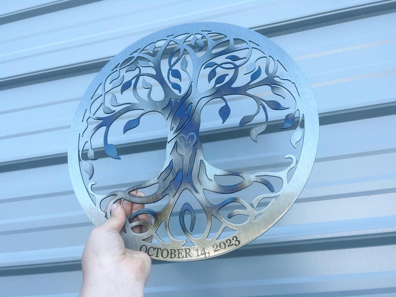 Peut inclure: Une d&eacute;coration murale en m&eacute;tal argent&eacute; en forme d'arbre de vie avec un motif de c&oelig;ur au centre et la date "OCTOBER 14, 2023" inscrite en dessous.