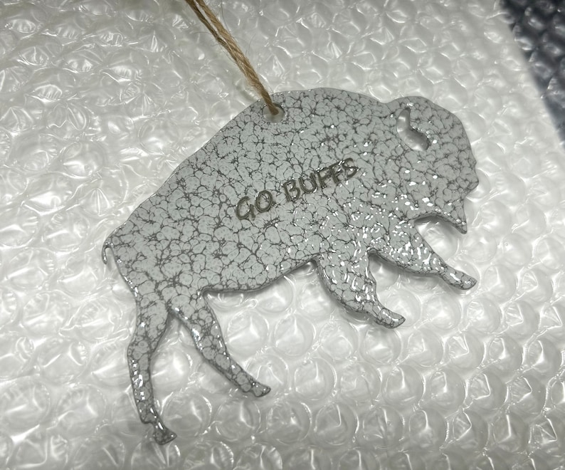 May include: White ceramic buffalo ornament with a distressed finish. The ornament has the words "Go Buffs" written on it.