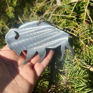 May include: A silver metal ornament shaped like a buffalo, hanging from a tree branch.