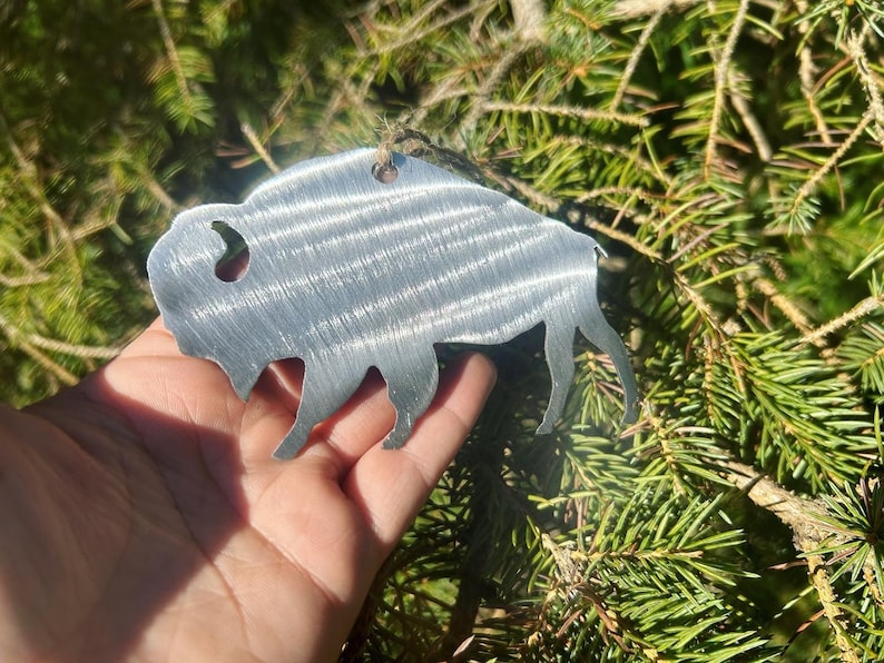 May include: A silver metal ornament shaped like a buffalo, hanging from a tree branch.