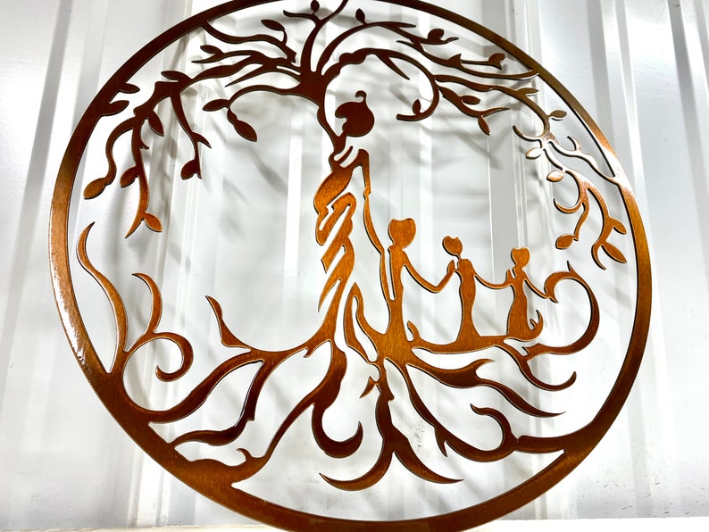 Puede incluir: Una pieza de arte de pared de metal que representa un &aacute;rbol de la vida estilizado con una familia de cuatro personas de pie debajo de sus ramas. El &aacute;rbol es marr&oacute;n y las figuras est&aacute;n silueteados sobre un fondo blanco.