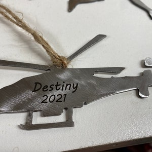 May include: A silver metal helicopter ornament with a twine hanger. The ornament is engraved with the text "Destiny 2021".