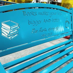 Puede incluir: Un banco de metal turquesa con un dise&ntilde;o recortado que presenta una pila de libros, una taza de caf&eacute; y el texto "Books make your life bigger AND better. Miss Marta, signing off 1957-2023."