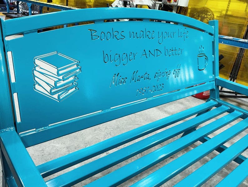 Puede incluir: Un banco de metal turquesa con un dise&ntilde;o recortado que presenta una pila de libros, una taza de caf&eacute; y el texto "Books make your life bigger AND better. Miss Marta, signing off 1957-2023."