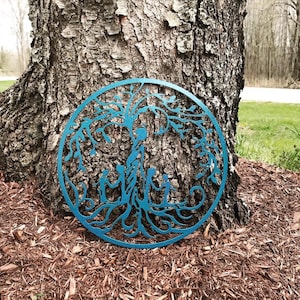 Puede incluir: Una decoraci&oacute;n de pared de metal azul en forma de &aacute;rbol de la vida con una familia de cinco figuras en el centro. El &aacute;rbol tiene ramas y ra&iacute;ces intrincadas.