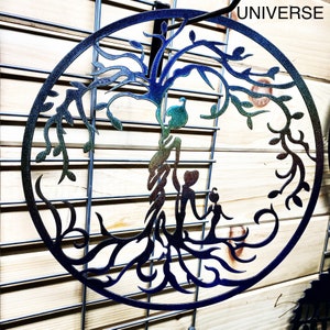 Puede incluir: Una decoraci&oacute;n de pared de metal en forma de &aacute;rbol de la vida con un acabado arco&iacute;ris iridiscente. El &aacute;rbol tiene una familia de tres figuras de pie en su base. Las palabras "UNIVERSE" est&aacute;n impresas en la esquina superior derecha de la imagen.