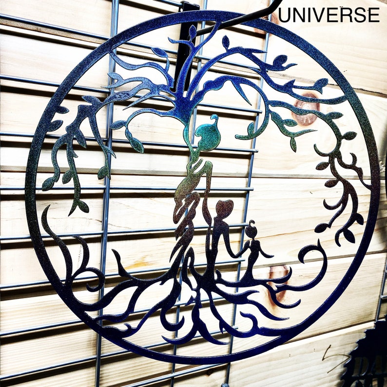 Puede incluir: Una decoraci&oacute;n de pared de metal en forma de &aacute;rbol de la vida con un acabado arco&iacute;ris iridiscente. El &aacute;rbol tiene una familia de tres figuras de pie en su base. Las palabras "UNIVERSE" est&aacute;n impresas en la esquina superior derecha de la imagen.