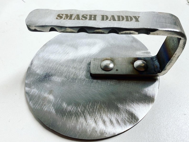 May include: A silver metal burger smasher with a handle. The handle has the words "SMASH DADDY" engraved on it.