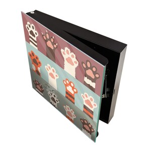 May include: A black box with a hinged lid, the lid is open and reveals a colorful glass panel with a pattern of cat paws in orange, white, and brown on a blue, pink, and green background.
