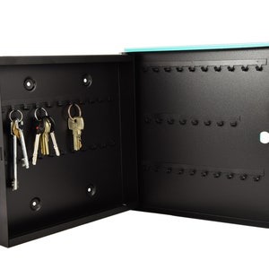 May include: A black metal key holder with a turquoise door. The key holder has 30 hooks and is open to reveal several keys hanging on the hooks.