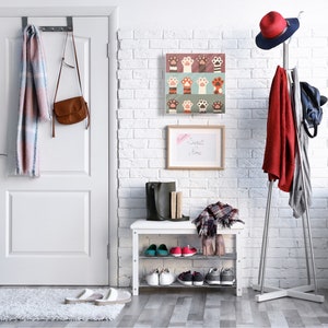 May include: A white brick wall with a white door, a shoe rack with shoes, a coat rack with a red coat, a hat, and a bag, and a framed print with paw prints. The print has a white background with colorful paw prints in various colors and patterns. The text "Sweet Dreams" is written on a white board hanging on the wall.