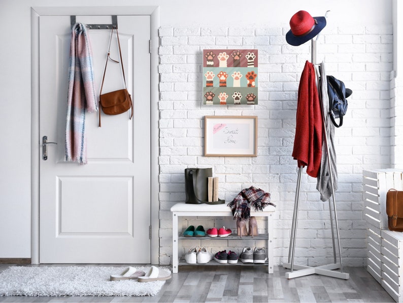 May include: A white brick wall with a white door, a shoe rack with shoes, a coat rack with a red coat, a hat, and a bag, and a framed print with paw prints. The print has a white background with colorful paw prints in various colors and patterns. The text "Sweet Dreams" is written on a white board hanging on the wall.