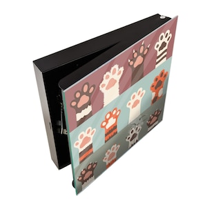 May include: A black box with a hinged lid, the lid is open and reveals a colorful design of cat paws on the inside. The paws are in a variety of colors and patterns, including orange, white, brown, and black.