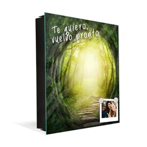 May include: A framed glass print with a photo of a path leading through a forest with a bright light at the end. The text "Te quiero, vuelvo pronto" is written on the print. A photo of three people is attached to the print with magnets.