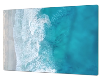 May include: An aerial view of a sandy beach meeting the turquoise ocean. White foamy waves crash against the shore, creating a beautiful contrast of colors.