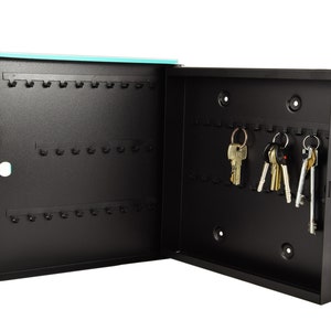 May include: A black metal key holder with a turquoise door. The key holder has multiple hooks for hanging keys. There are several keys hanging on the hooks.