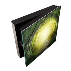 May include: A black framed wall art piece with a green and yellow image of a path through a forest. The image is printed on glass and the frame is open on one side.