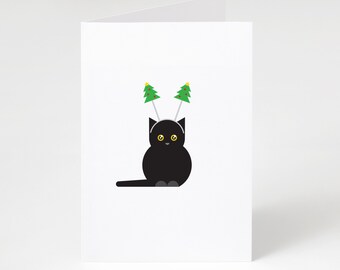 Puede incluir: Una tarjeta de felicitación blanca plegada con un gato negro de dibujos animados que lleva una diadema con dos árboles de Navidad verdes. El gato tiene ojos amarillos y patas grises. La tarjeta está en blanco por dentro.