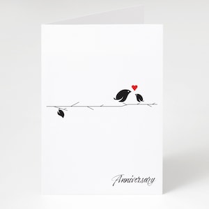 May include: A white anniversary card with a minimalist design. It features two black birds on a branch, a red heart, and the word "Anniversary" in script. The card is blank inside.