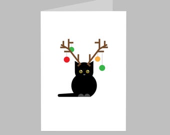 Peut inclure: Carte de Noël avec un chat noir portant des bois bruns ornés de boules rouges, vertes et jaunes. Le chat a des yeux jaunes et se détache sur un fond blanc.