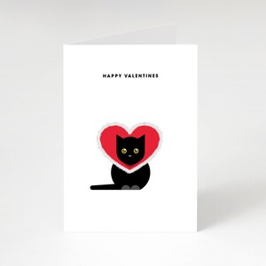 May include: A Valentine's Day card with a black cat wearing a red heart-shaped collar with white trim. The words "HAPPY VALENTINES" are printed at the top of the white card. The cat has yellow eyes.