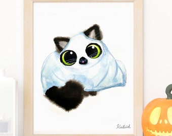 May include: A watercolour painting of a black and white cat dressed as a ghost for Halloween. The cat has large green eyes and is looking directly at the viewer. The painting is framed in a light wood frame and is hanging on a white wall.