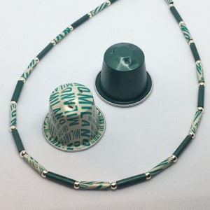 May include: A green and white necklace made of coffee pods with a green and white coffee pod lid on a white surface.