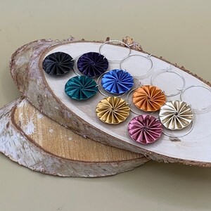 May include: A set of eight colorful, patterned earrings with silver hoops. The earrings are made of folded paper and feature a variety of colors, including blue, green, gold, and pink.