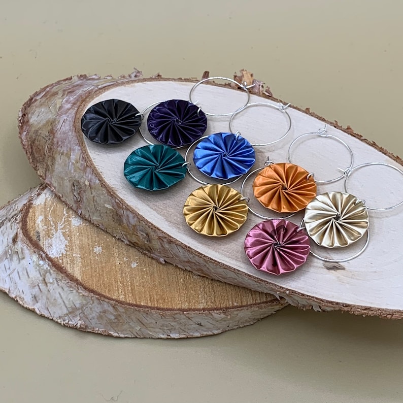 May include: A set of eight colorful, patterned earrings with silver hoops. The earrings are made of folded paper and feature a variety of colors, including blue, green, gold, and pink.