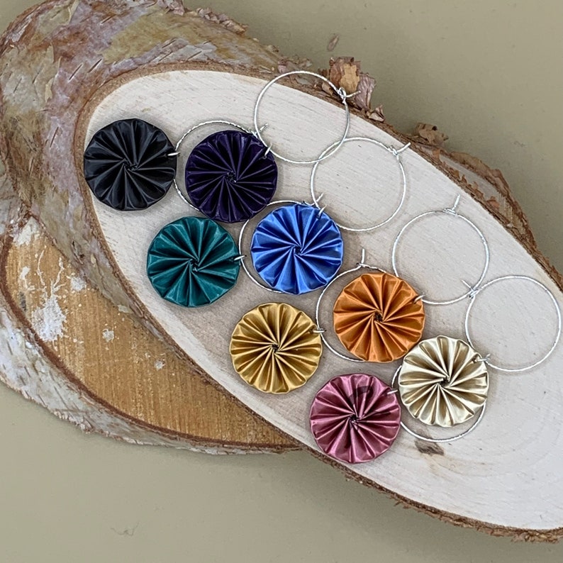 May include: A set of eight earrings featuring colorful, swirling, circular designs. The earrings are attached to silver hoops.