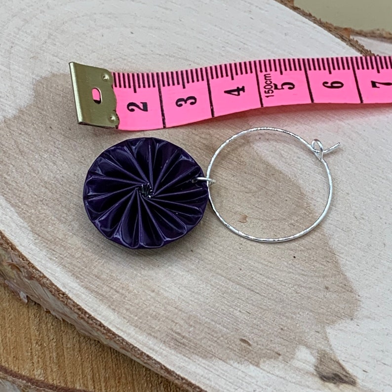 May include: A pair of earrings with a dark purple, circular, origami-style design hanging from silver hoops.