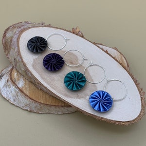 May include: Four pairs of silver hoop earrings with different colored fabric flower accents. The colors are black, dark purple, teal, and blue.
