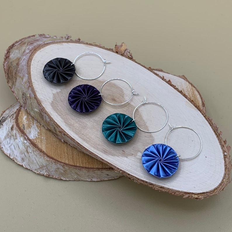 May include: Four pairs of silver hoop earrings with different colored fabric flower accents. The colors are black, dark purple, teal, and blue.